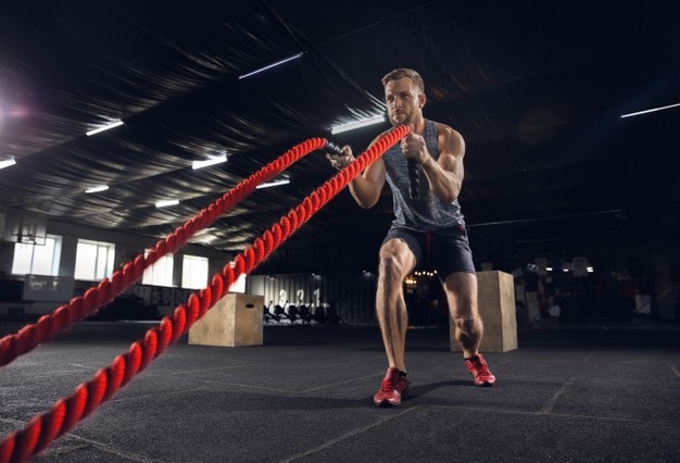 Young healthy man, athlete doing exercise with the ropes in gym