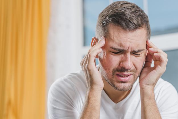 man grimacing in pain touching his head with fingers