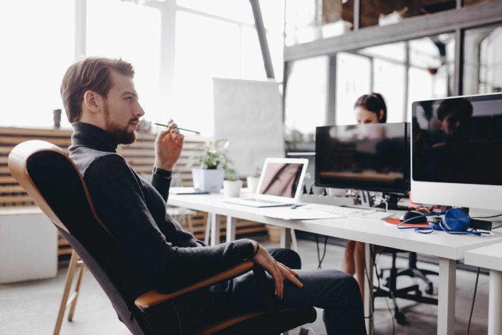 The guy dressed in casual office style clothes is sitting in an office chair at desk in the modern office