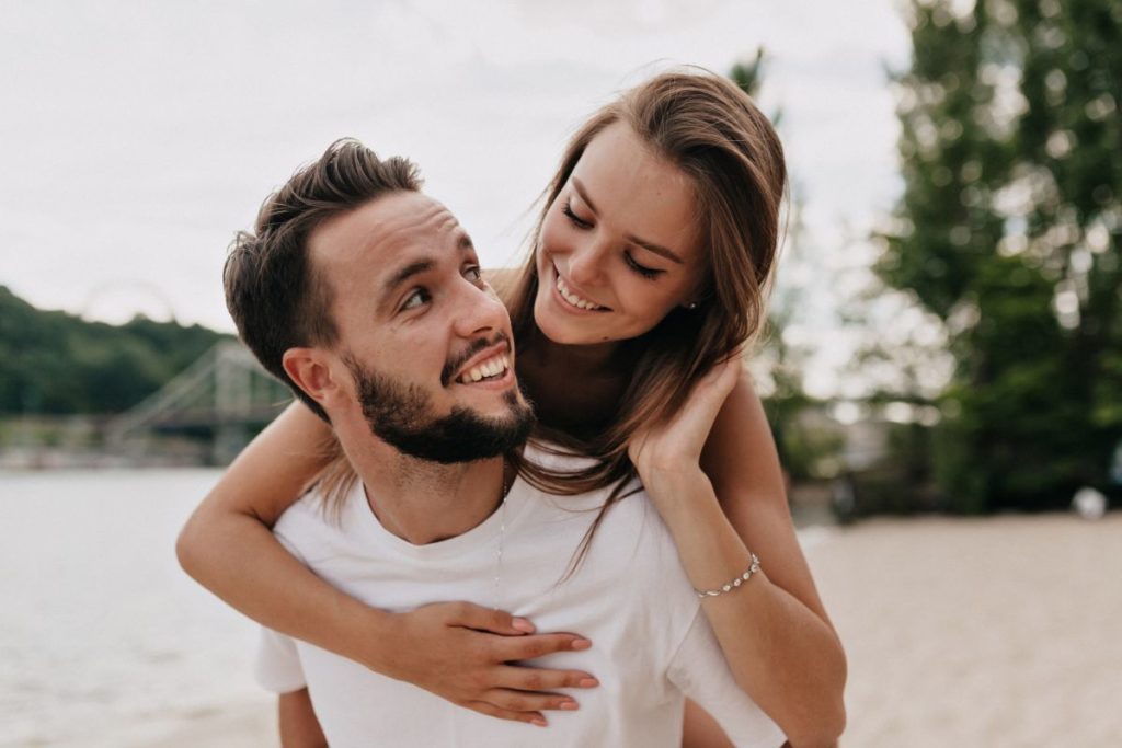 Beautiful young couple is talking and smiling while walking on the beach in sunny day 