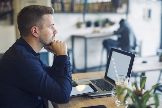 businessman sitting in cafe bar with laptop being worried and thinking about solution for his problem