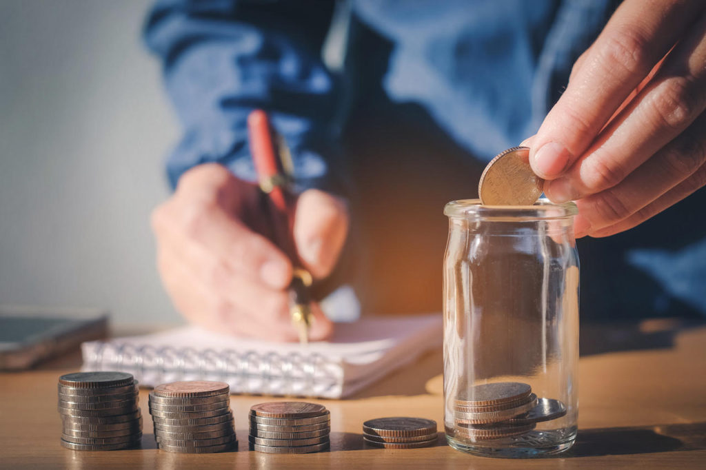 Man putting money into small glass jar 