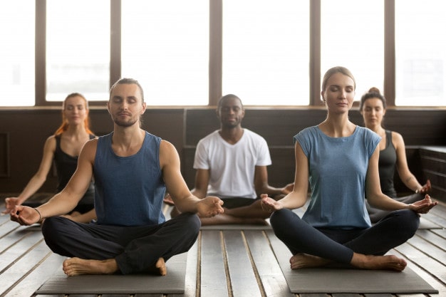 Group of young sporty people sitting in sukhasana exercise 