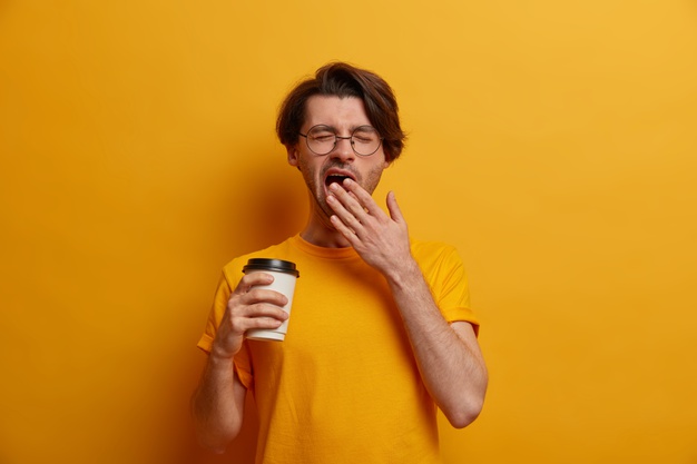 man holding coffe cup and yawning