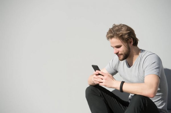 Bearded man use mobile phone on grey wall
