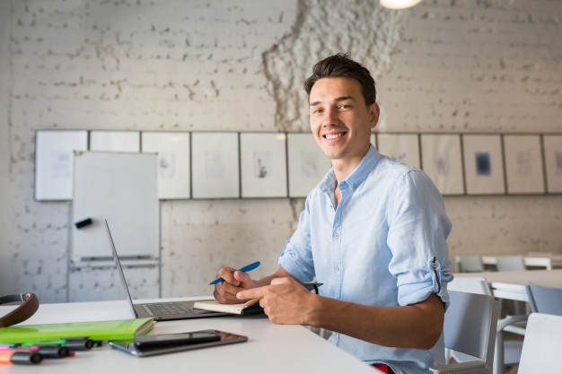 Happy remote worker young handsome man thinking, writing notes in notebook 