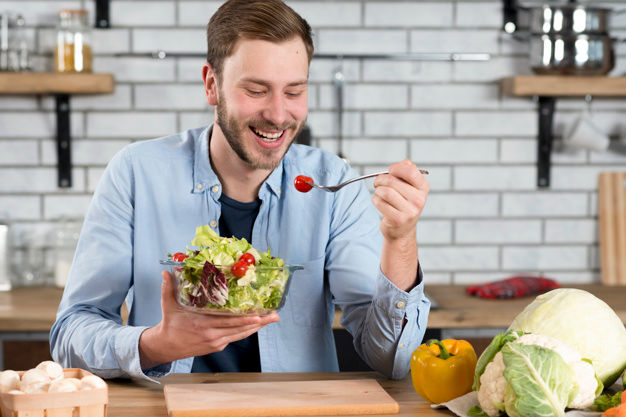 happy man eating fresh salad in the kitchen