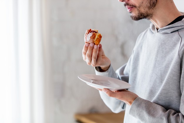 Man eating donut on breakfast at kitchen at home