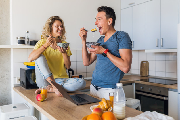 couple of man and woman eating breakfast together in morning at kitchen