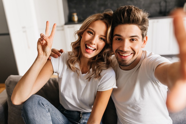 young couple at home making selfie with peace sign and smiling widely