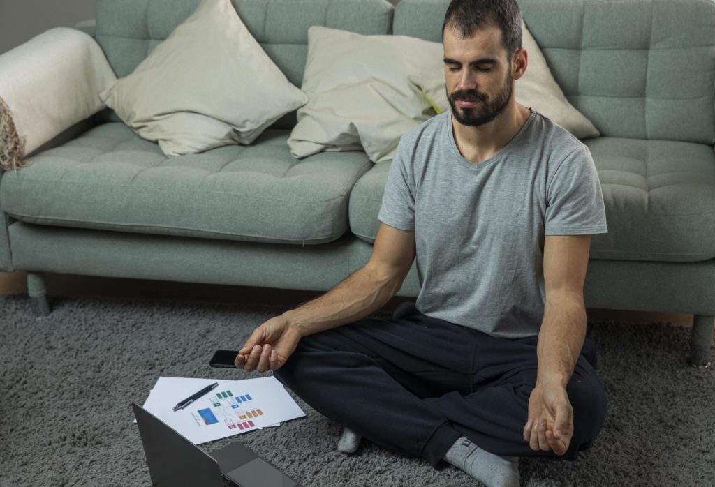 Man meditating next to sofa before starting work 