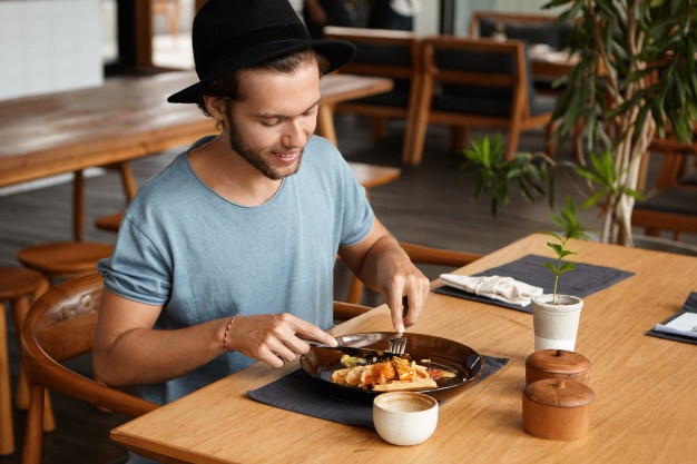 man with beard smiling happily as he eating some tasty food with knife and fork