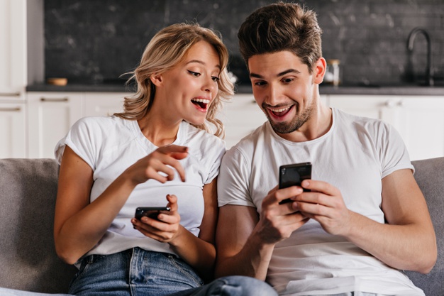 happy couple sitting on sofa and using phone