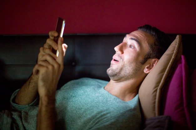 man using phone on sofa at night