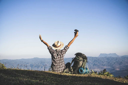 Tourist from mountain top. sun rays. man wear big backpack against sun light