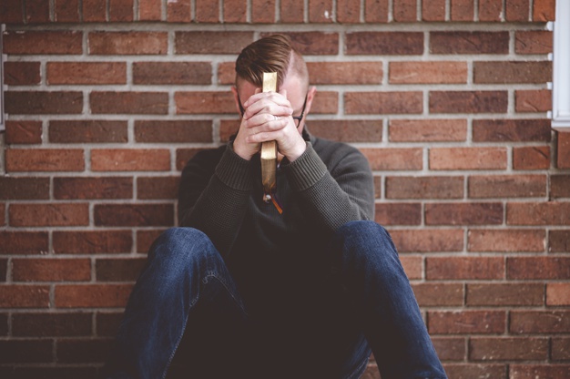 Depressed young male sitting on the ground on a wall holding the holy bible