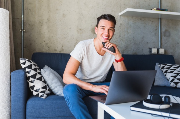 man sitting on sofa at home working on laptop online,