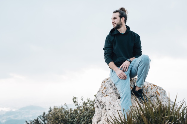 Young man sitting on top of rock looking