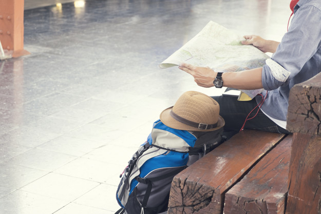 Traveler wearing backpack holding map, waiting for a train at trainstation and planing for next trip