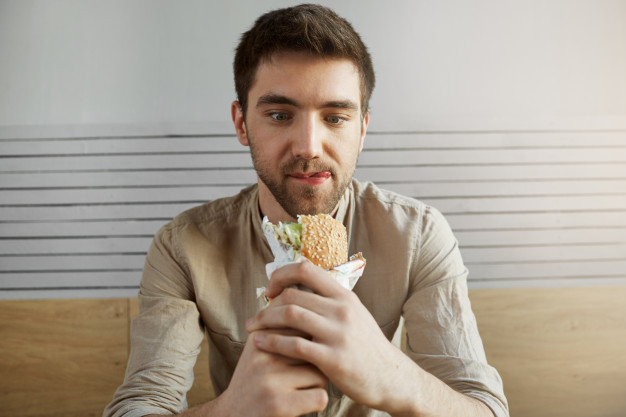 dark haired guy sitting in cafe, looking with happy expression at sandwich, 