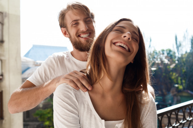 Beautiful couple standing at balcony. man making massage his girlfriend.