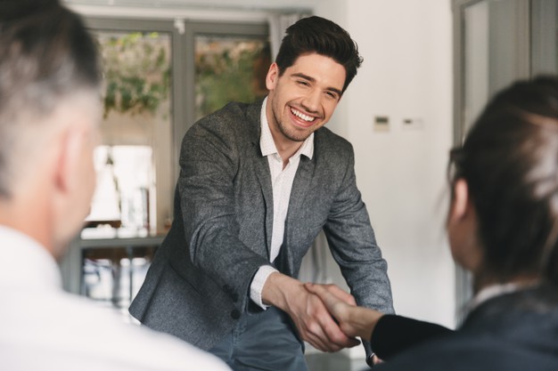 career and placement concept - happy european man wearing suit rejoicing and shaking hands with group of employee