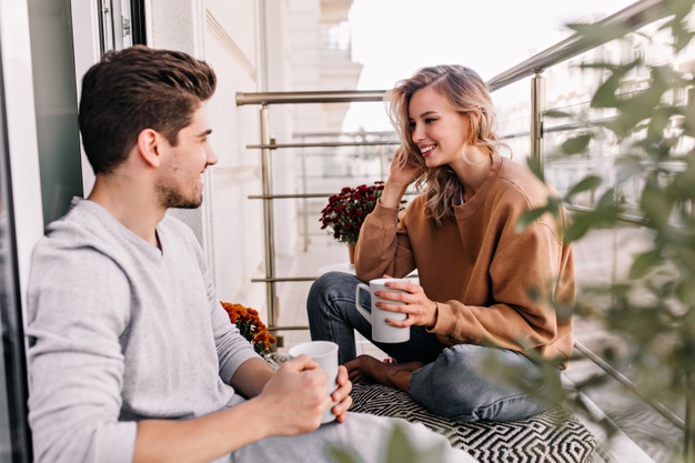 Cheerful lady talking with husband at balcony. charming young woman drinking tea at terrace
