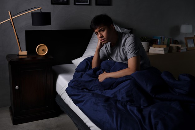 man suffering from insomnia sitting in bed 