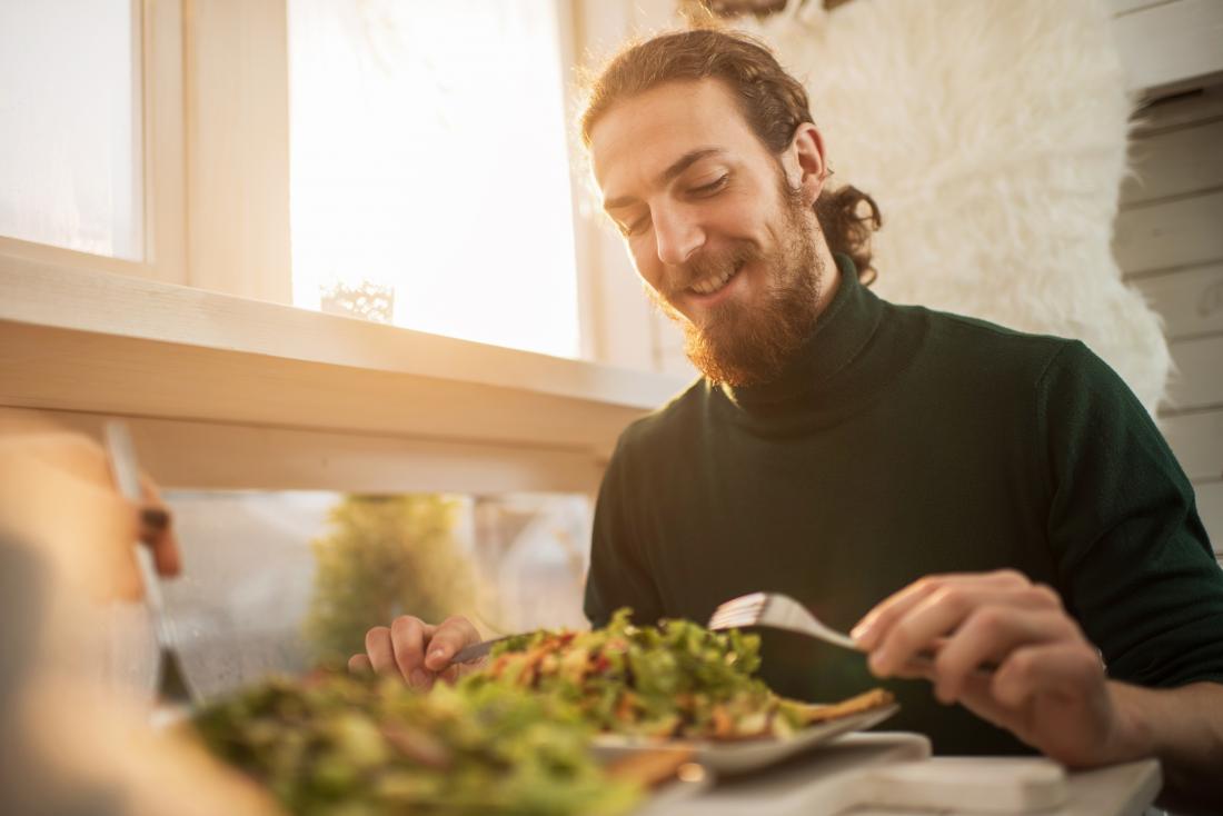 happy man eating fresh salad in the kitchen