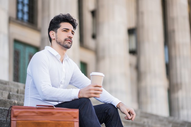 business man drinking a cup of coffee on a break from work while sitting on stairs outdoors