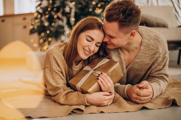 Young couple making gifts to each other by the christmas tree 