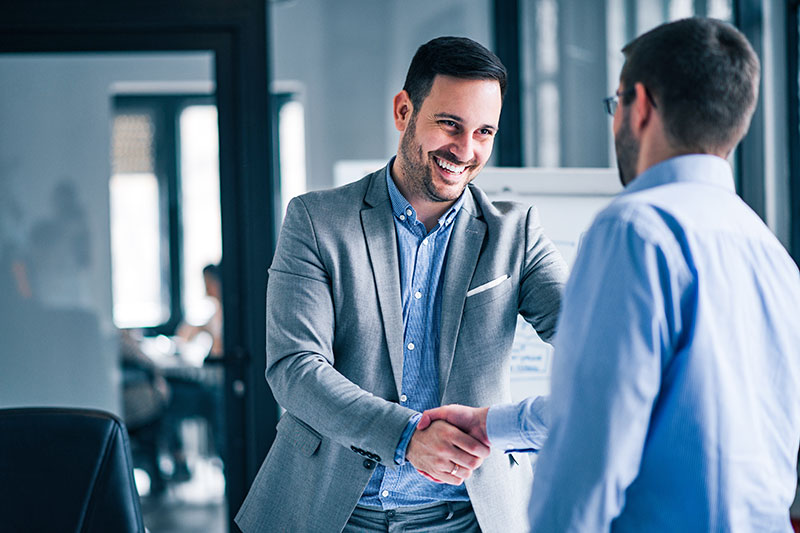 two-smiling-businessmen-shaking-hands-while-standing-office