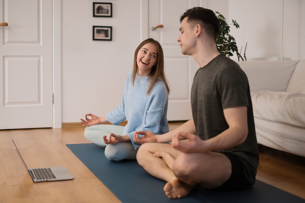 couple practicing yoga together at home using a laptop taking online yoga classes