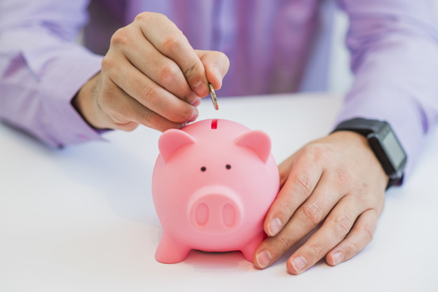 the hand of a man placing a coin into the slot of a piggy bank in a savings and investment
