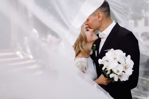Groom in black tuxedo hugs tender stunning bride while they stand 