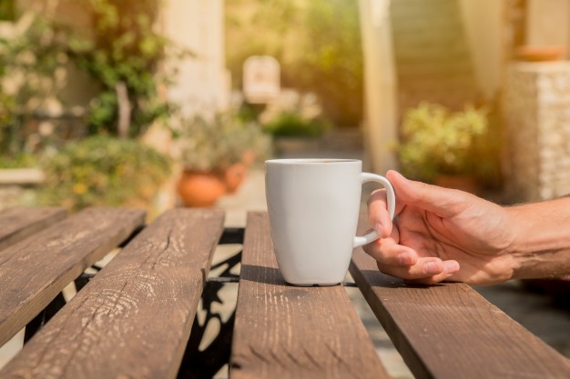 hand-is-holding-coffee-cup-men-are-drinking-morning-coffee-with-green-background-outside-man-hands-holding-cup-coffee-cafe-outdoors-summer