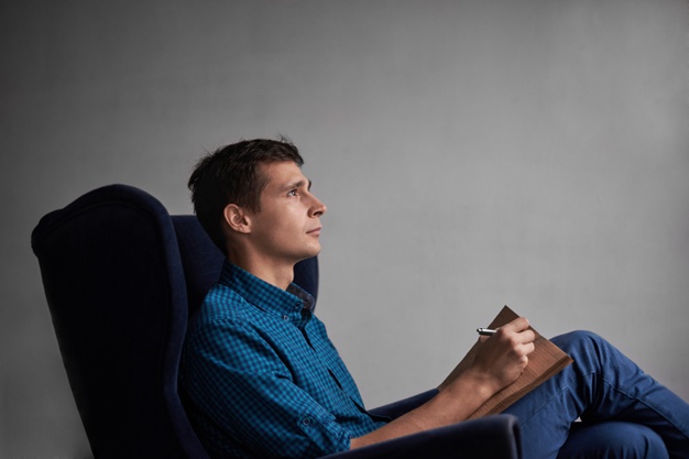 handsome-man-blue-shirt-jeans-sitting-dark-chair-write-ideas-notepad