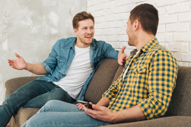 man sitting on sofa talking to his friend holding mobile in hand 
