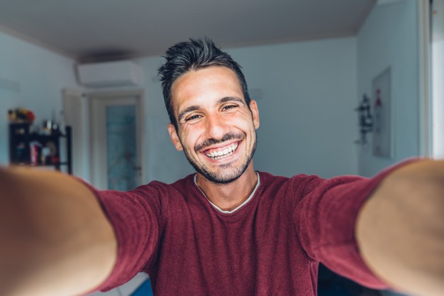 happy-young-handsome-millennial-taking-selfie-smiling-living-room-home