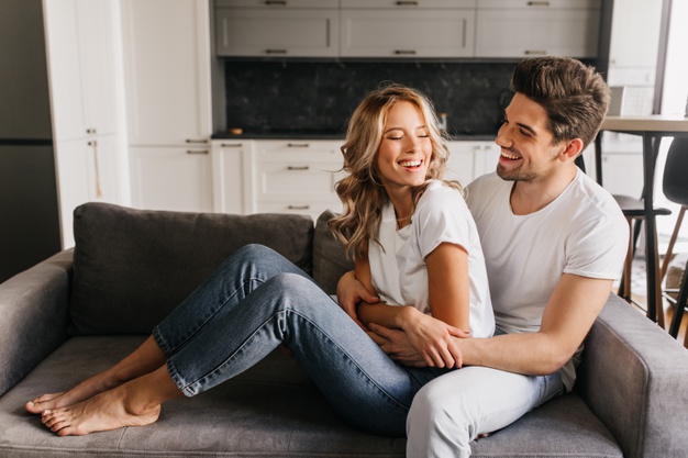 happy attractive guy with beautiful girl looking at each other laughing and hugging on sofa
