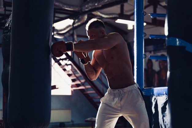 Male boxer training with punching bag in dark sports hall. young boxer training on punching bag.