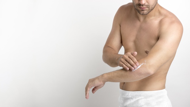 Shirtless young man applying cream on hand against white