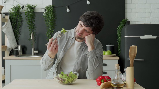unhappy-man-eating-vegetable-salad-table-kitchen