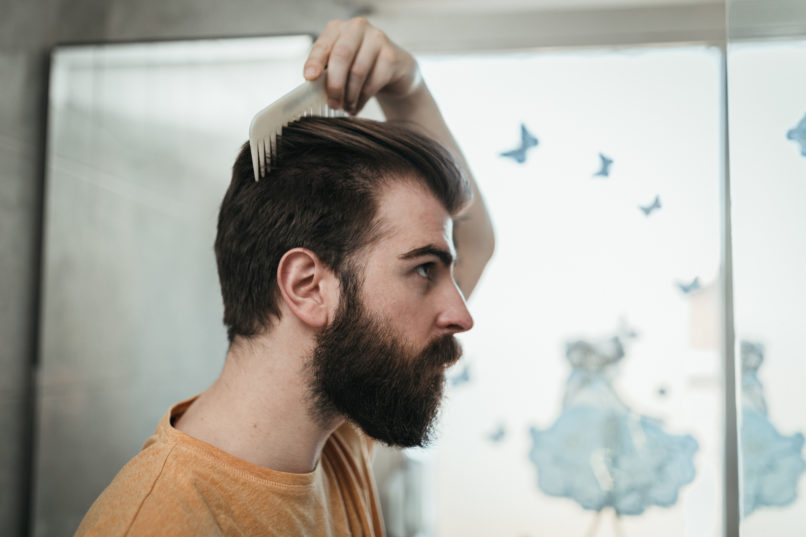 Handsome bearded man combing his hair in the bathroom in the morning