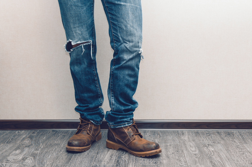 Young fashion man's legs in jeans and boots on wooden floor