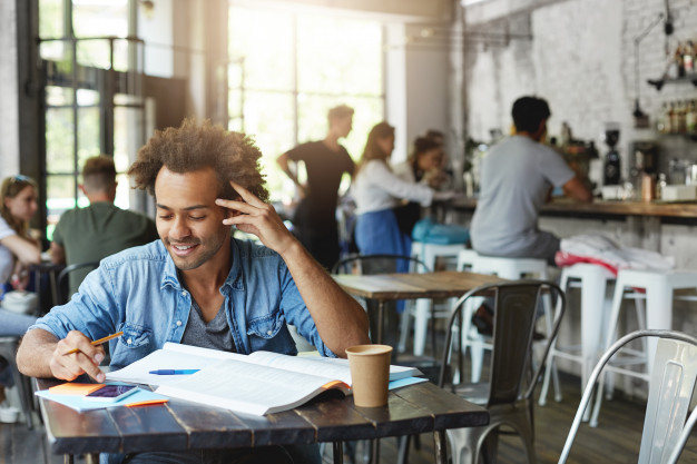 student with stylish afro haircut smiling broadly while reading message on cell phone