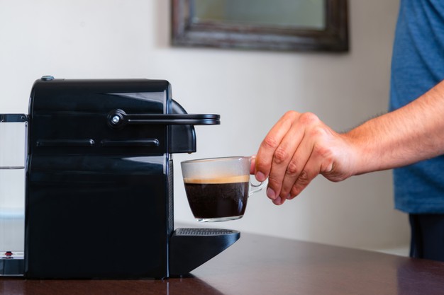 hand picking up a cup of espresso of capsule coffee machine at home