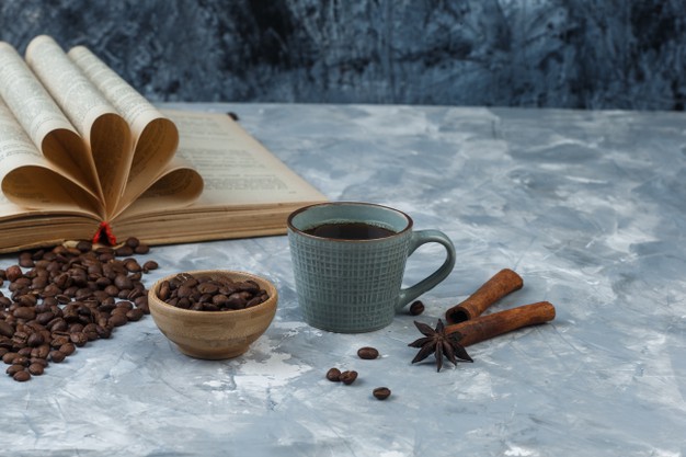 coffee-beans-wooden-bowl-with-book-cinnamon-cup-coffee-high-angle-view-light-dark-blue-marble-background