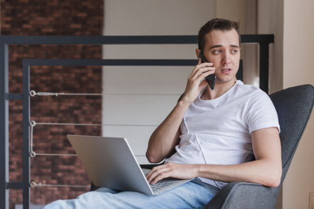 Concentrated man talking on mobile phone and sitting on chair with laptop