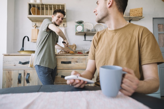 man working in kitchen looking at his friend using mobile phone